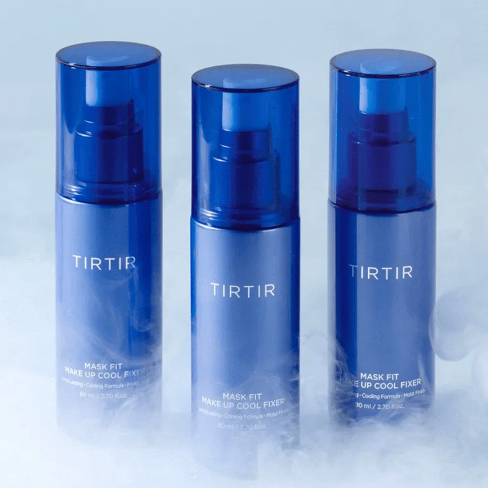 Três frascos de spray azuis com "TIRTIR Mask Fit Make Up Cool Fixer" no rótulo. Cada frasco contém 80 ml (2,70 fl. oz.) e é projetado para proporcionar uma sensação refrescante e maquiagem duradoura. Os frascos estão posicionados sobre um fundo claro com névoa para criar uma atmosfera de frescor.