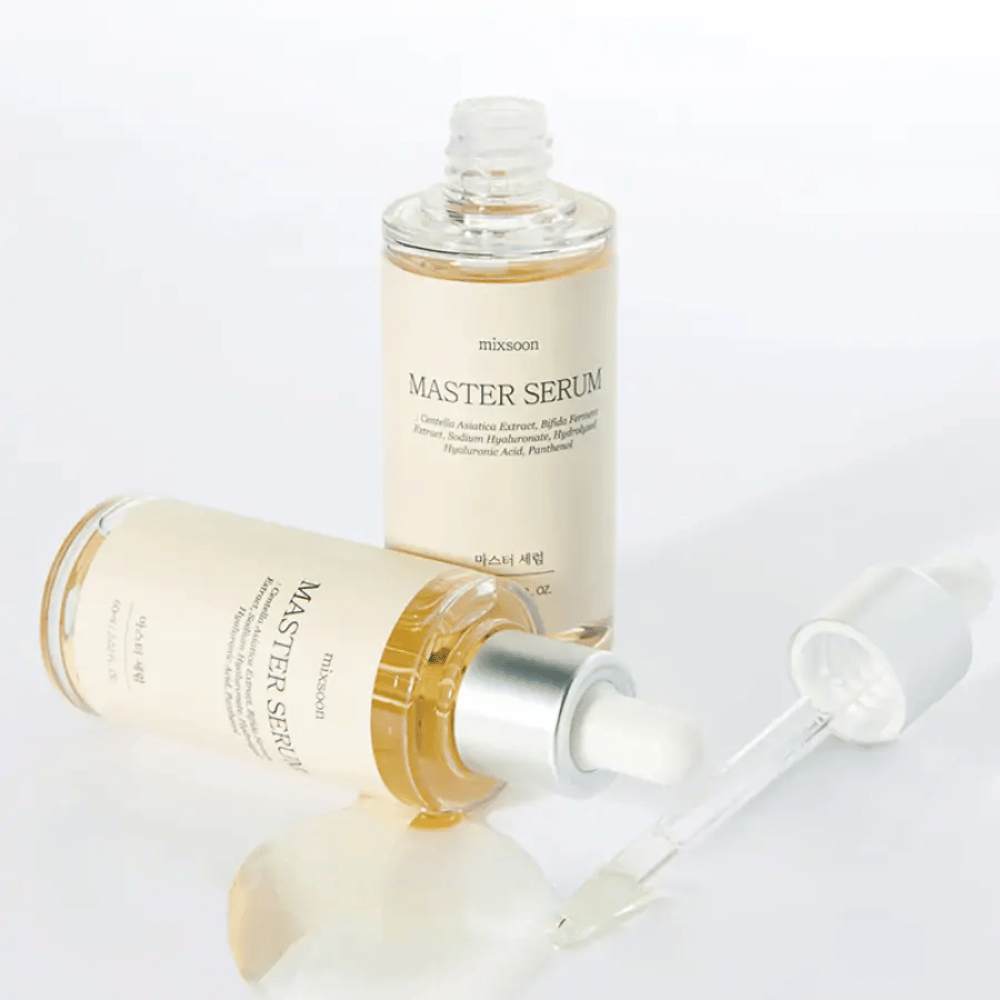 Duas garrafas Mixsoon Master Serum, uma em pé e outra deitada com conta-gotas aberto, onde o soro foi derramado sobre uma superfície branca.
