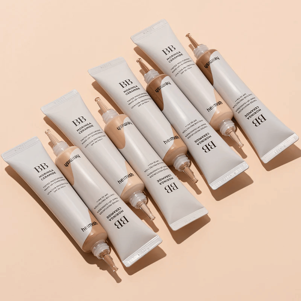 Vários tubos de Heimish Moringa Ceramide BB Cream dispostos sobre um fundo bege claro. A imagem realça os diferentes tons e o design elegante e minimalista da embalagem do produto.