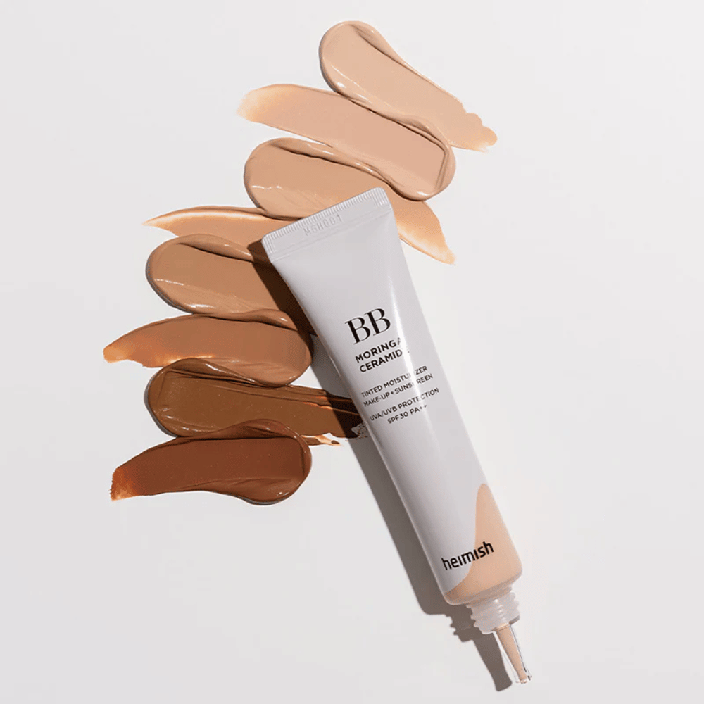 Heimish Moringa Ceramide BB Cream rodeado por várias amostras de tons em diferentes tonalidades de pele. A imagem mostra a ampla gama de cores do produto e a textura cremosa que proporciona uma cobertura natural e um tom de pele uniforme.