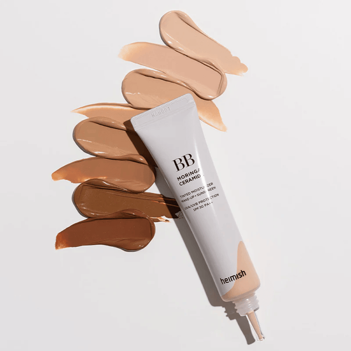 Heimish Moringa Ceramide BB Cream rodeado por várias amostras de tons em diferentes tonalidades de pele. A imagem mostra a ampla gama de cores do produto e a textura cremosa que proporciona uma cobertura natural e um tom de pele uniforme.