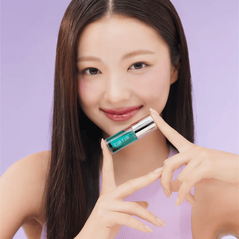Mulher com cabelo longo e liso segurando TIRTIR My Glow Lip Oil e exibindo seus lábios brilhantes e rosados contra um fundo roxo.