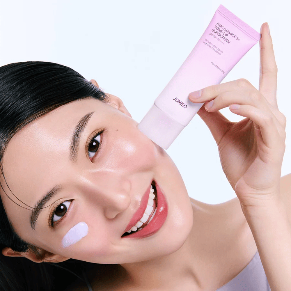 A modelo aplica JUMISO Niacinamide 3+ Tone-Up Sunscreen SPF50+ PA++++ para proteção UV, tom de pele mais uniforme e luminosidade natural.