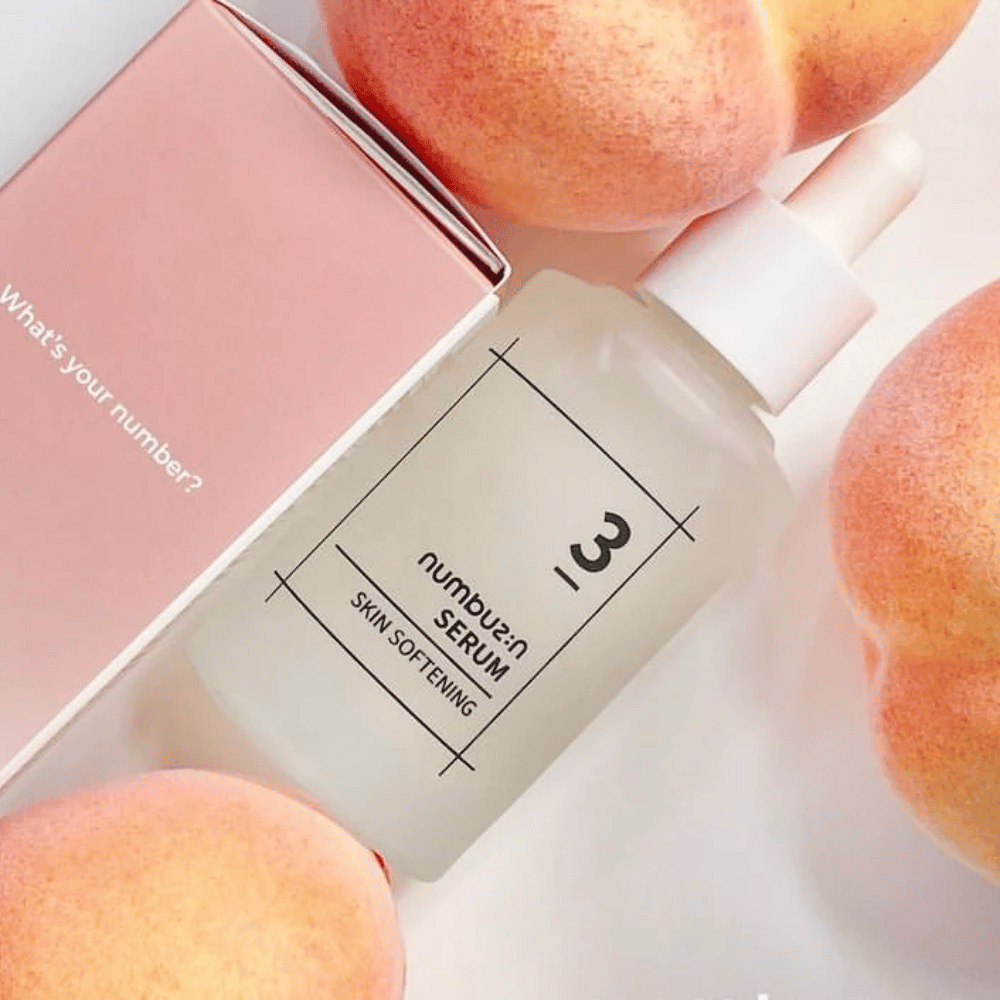 Frasco com numbus:in No.3 Skin Softening Serum rodeado por pêssegos e uma caixa rosa com o texto "Qual é o seu número?".