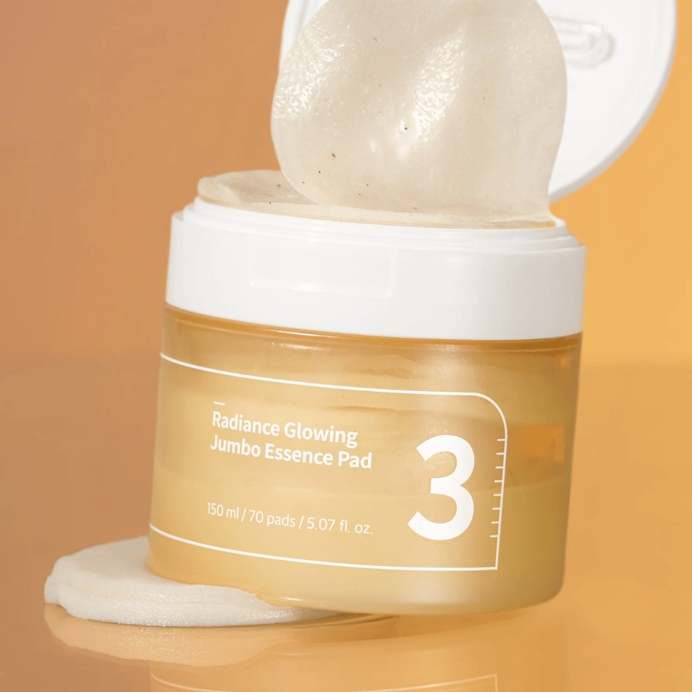 Frasco aberto com numbuzin No. 3 Radiance Glowing Jumbo Essence Pad, um pad visível inclinado contra a borda, fundo em tom laranja.