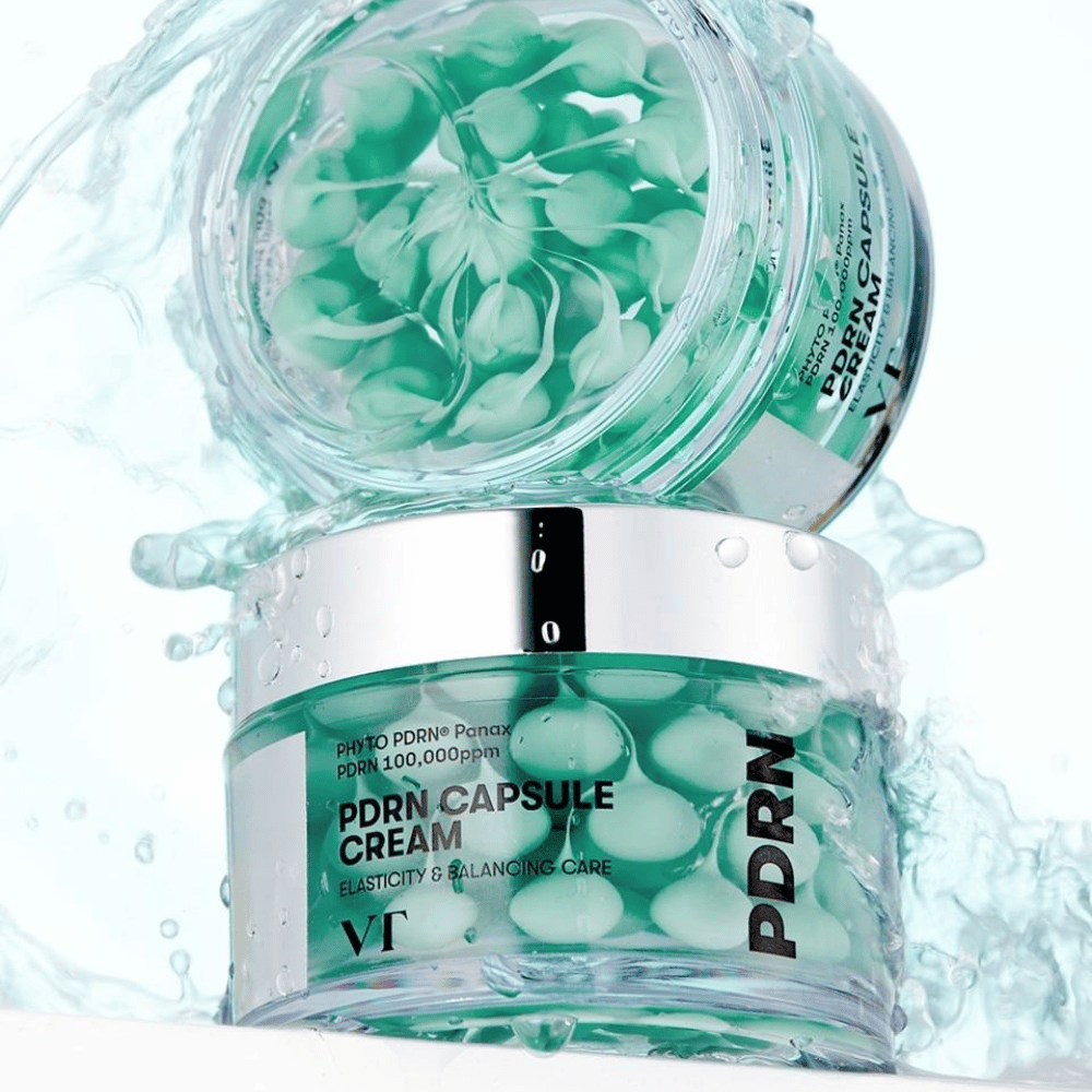 Dois frascos de VT PDRN Capsule Cream empilhados com respingos de água ao redor. Os frascos transparentes mostram cápsulas verdes dentro, com o texto "Elasticity & Balancing Care" visível no rótulo.
