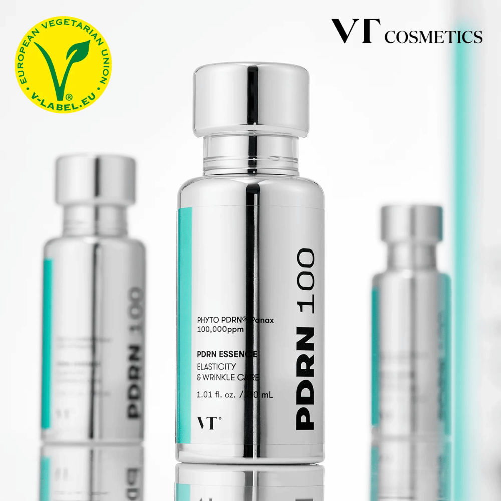 Vários frascos prateados de VT PDRN 100 Essence estão alinhados, com marcação clara de 100,000 ppm PDRN e foco em elasticidade e cuidado com rugas. No topo, vê-se o logotipo de VT Cosmetics e um rótulo V para conteúdo vegetariano.