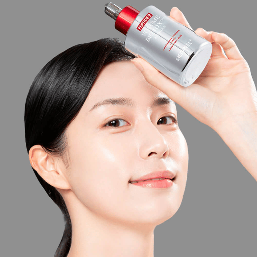 Pessoa segurando o MEDI-PEEL Peptide 9 Volume Bio Tox Pro Ampoule contra a testa. A pele parece hidratada e radiante – o sérum reforça a elasticidade e firmeza.