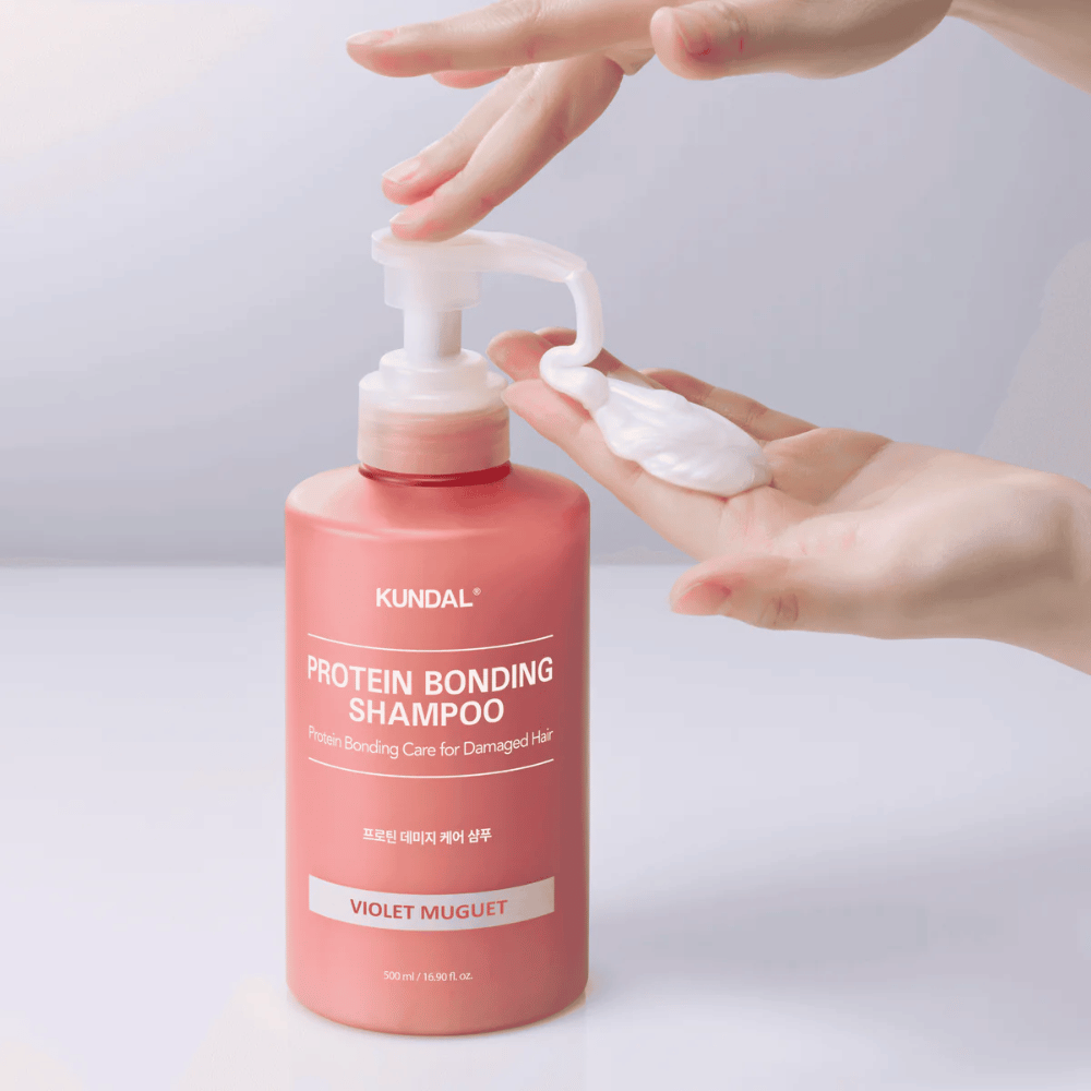 Mão bombeia KUNDAL Protein Bonding Shampoo Violet Muguet em consistência cremosa, shampoo reparador para cabelo danificado.