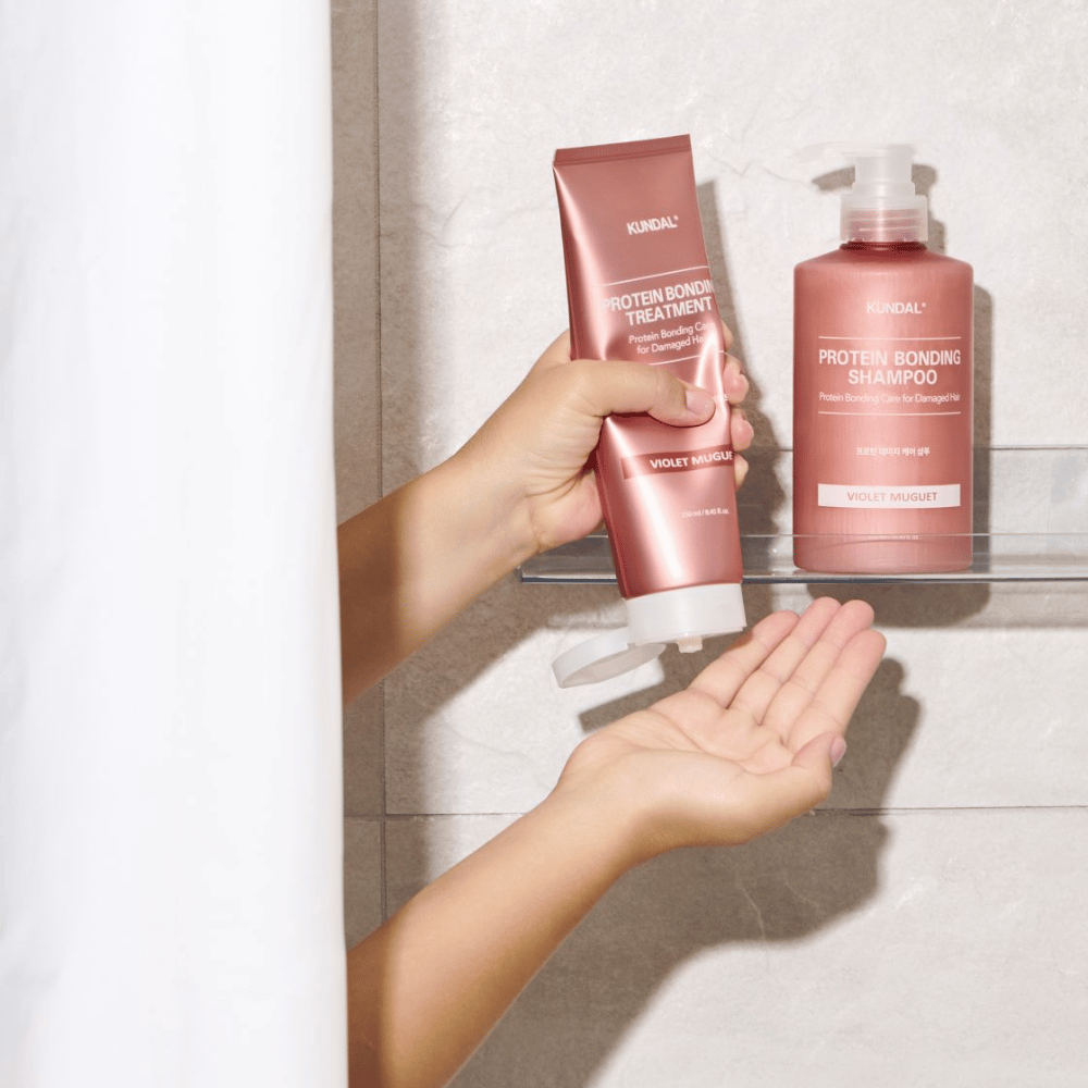 KUNDAL Protein Bonding Treatment Violet Muguet é usado no chuveiro, com Protein Bonding Shampoo colocado na prateleira ao lado.