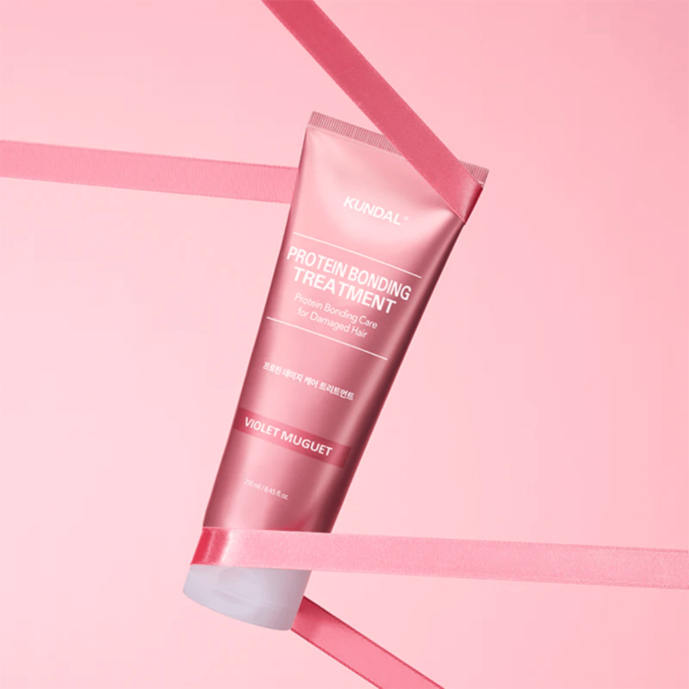 KUNDAL Protein Bonding Treatment Violet Muguet em tubo rosa 250 ml contra um fundo rosa com fitas decorativas.