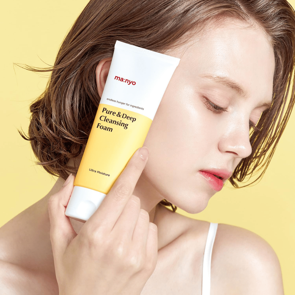 Mulher com pele saudável e hidratada segurando Ma:nyo Pure & Deep Cleansing Foam – limpeza facial suave que proporciona brilho e equilíbrio com ingredientes naturais.