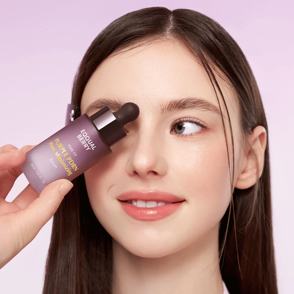 Jovem mulher com pele lisa segurando uma garrafa Equal Berry Purple PDRN Pore Minimizing Serum contra a testa, contra um fundo lilás claro.