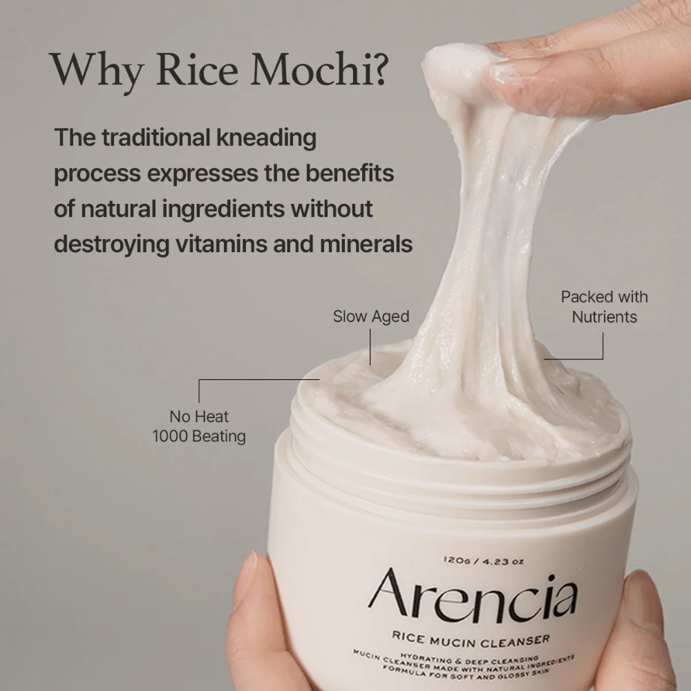 Mão levantando um creme de limpeza branco e elástico de um pote rotulado "Arencia Rice Mucin Cleanser". O texto descreve a amassadura tradicional que preserva nutrientes sem destruir vitaminas e minerais.