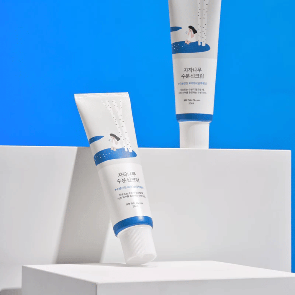 Dois tubos com Round Lab Birch Juice Moisturizing Sunscreen SPF50+ PA++++ 50ml que estão sobre um fundo azul.