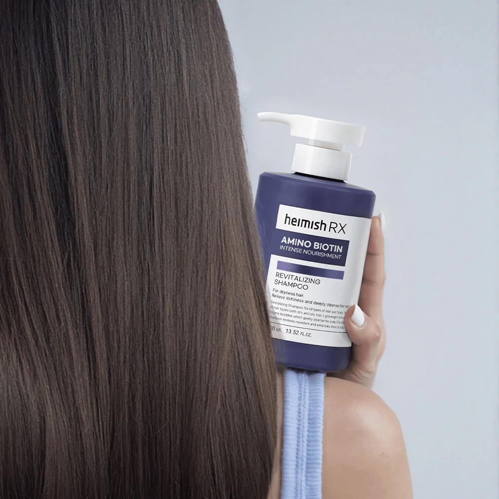 Heimish RX Amino Biotin Revitalizing Shampoo hålls i handen mot långt, glansigt hår – visar resultatet av intensiv näring och återfuktning för torrt hår.