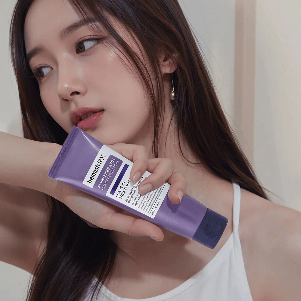 Mulher com cabelo comprido e brilhante segurando Heimish RX Amino Keratin Leave-In Treatment – mostra o produto como um passo cuidadoso e protetor térmico na rotina de cuidados capilares.