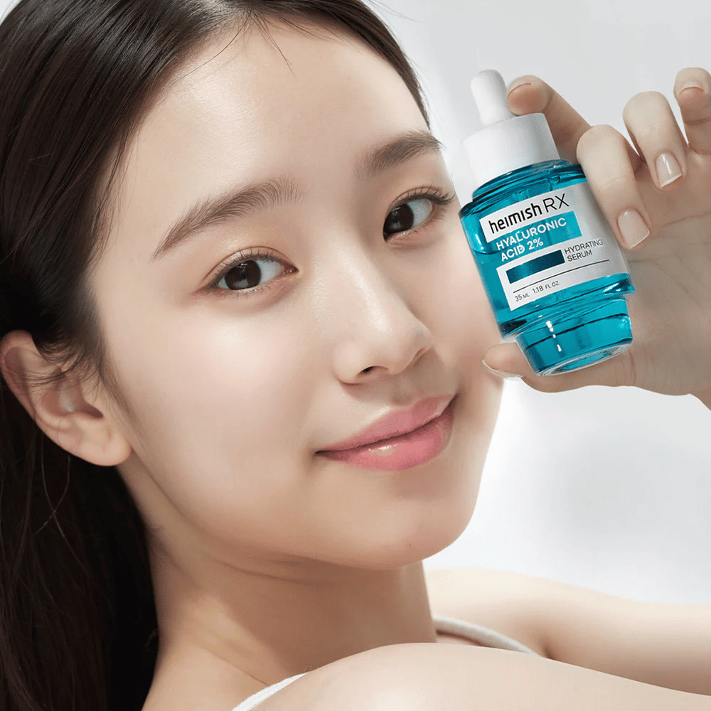 Mulher sorridente com pele radiante segurando um frasco de Heimish RX Ácido Hialurônico 2% Sérum Hidratante, destacando suas propriedades hidratantes.