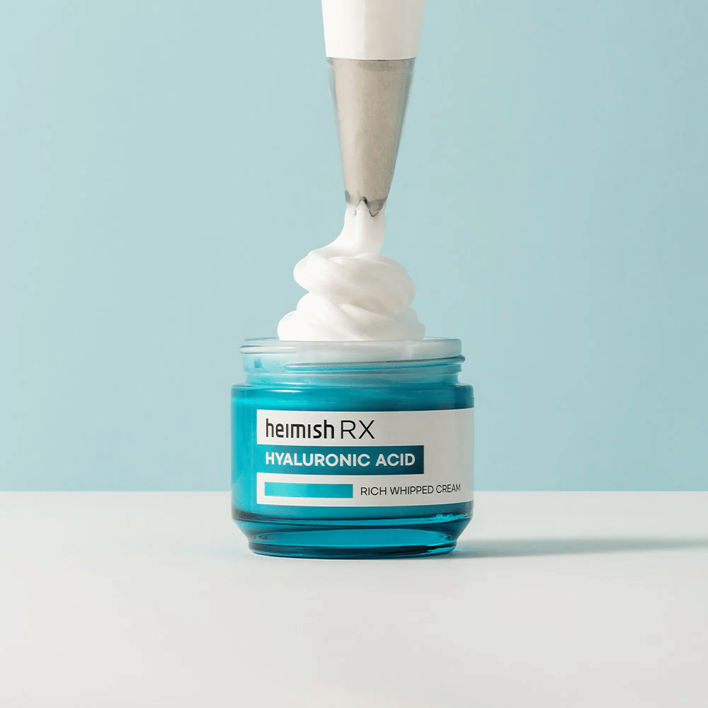 Heimish RX Hyaluronic Acid Rich Whipped Cream em um frasco de vidro azul, onde um saco de confeitar aplica o creme fofo. Um creme facial hidratante com ácido hialurônico para hidratação intensa e uma pele macia e preenchida.