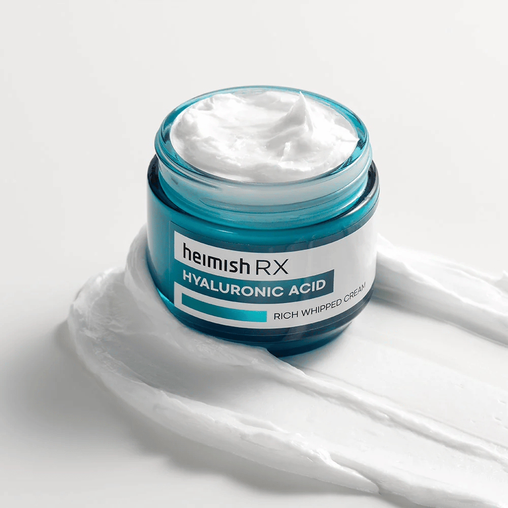 Heimish RX Hyaluronic Acid Rich Whipped Cream em um frasco de vidro azul com consistência rica e fofa, espalhado sobre um fundo branco. Creme facial intensamente hidratante com ácido hialurônico para hidratação profunda e pele macia.