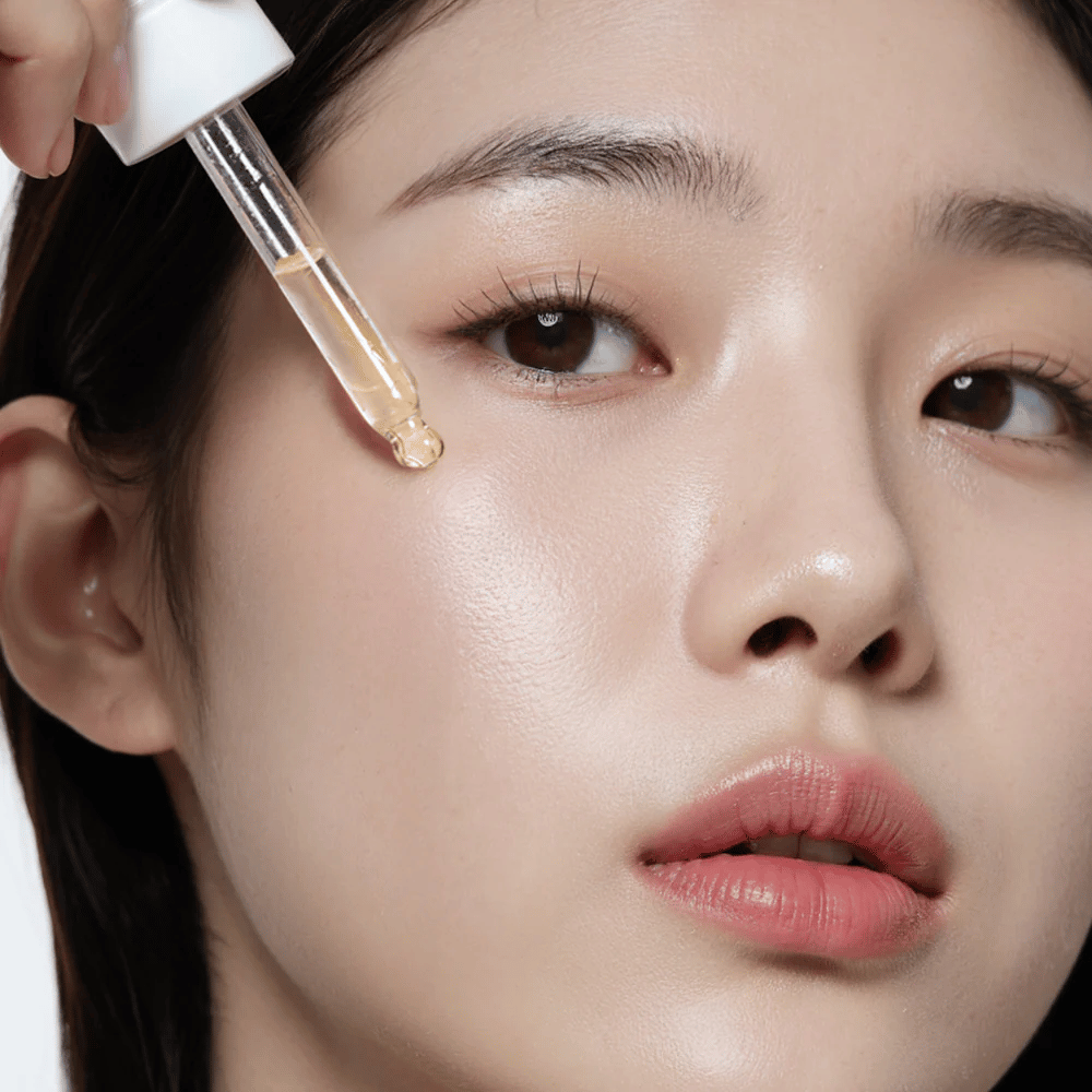 Close-up de uma mulher com pele lisa e hidratada aplicando Heimish RX Multi Vitamina 7% Glow Serum com uma pipeta para brilho e nutrição extra.