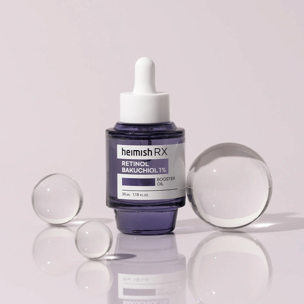 Heimish RX Retinol Bakuchiol Booster Oil 1% em uma elegante garrafa de vidro roxa com conta-gotas. O óleo está colocado em uma superfície refletora com esferas de vidro ao redor, proporcionando uma sensação luxuosa e moderna.