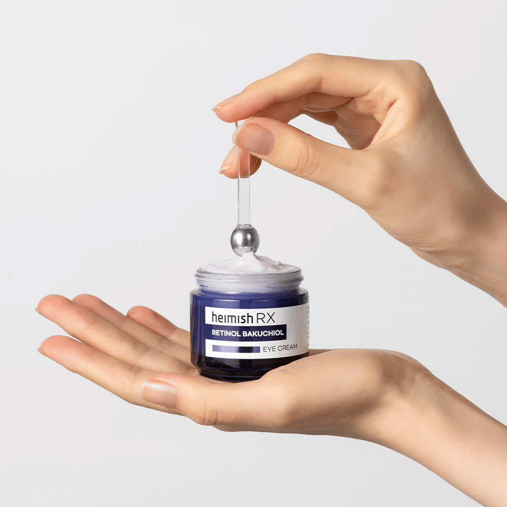 Heimish RX Retinol Bakuchiol Eye Cream em um frasco azul elegante, levantado com um aplicador de metal. Um creme para os olhos com retinol e bakuchiol para reduzir linhas finas e proporcionar uma pele mais firme.