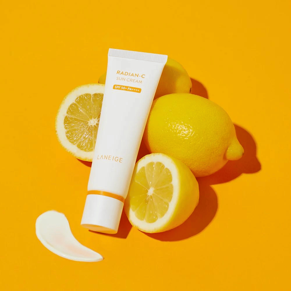 LANEIGE Radian-C Sun Cream SPF 50+ PA++++ com limões e um pouco de protetor solar sobre um fundo amarelo vibrante.