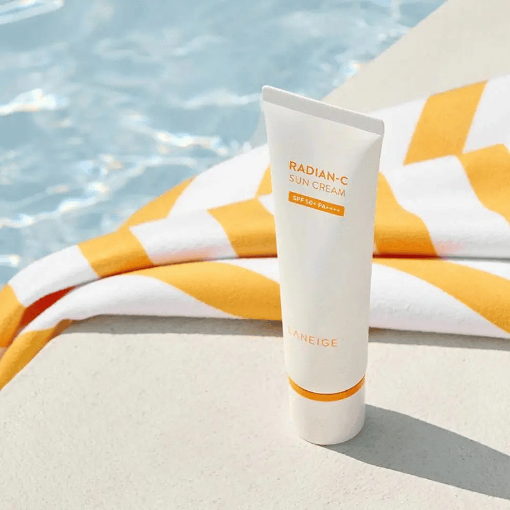 LANEIGE Radian-C Sun Cream está ao lado de uma piscina com uma toalha listrada de amarelo e branco ao fundo.