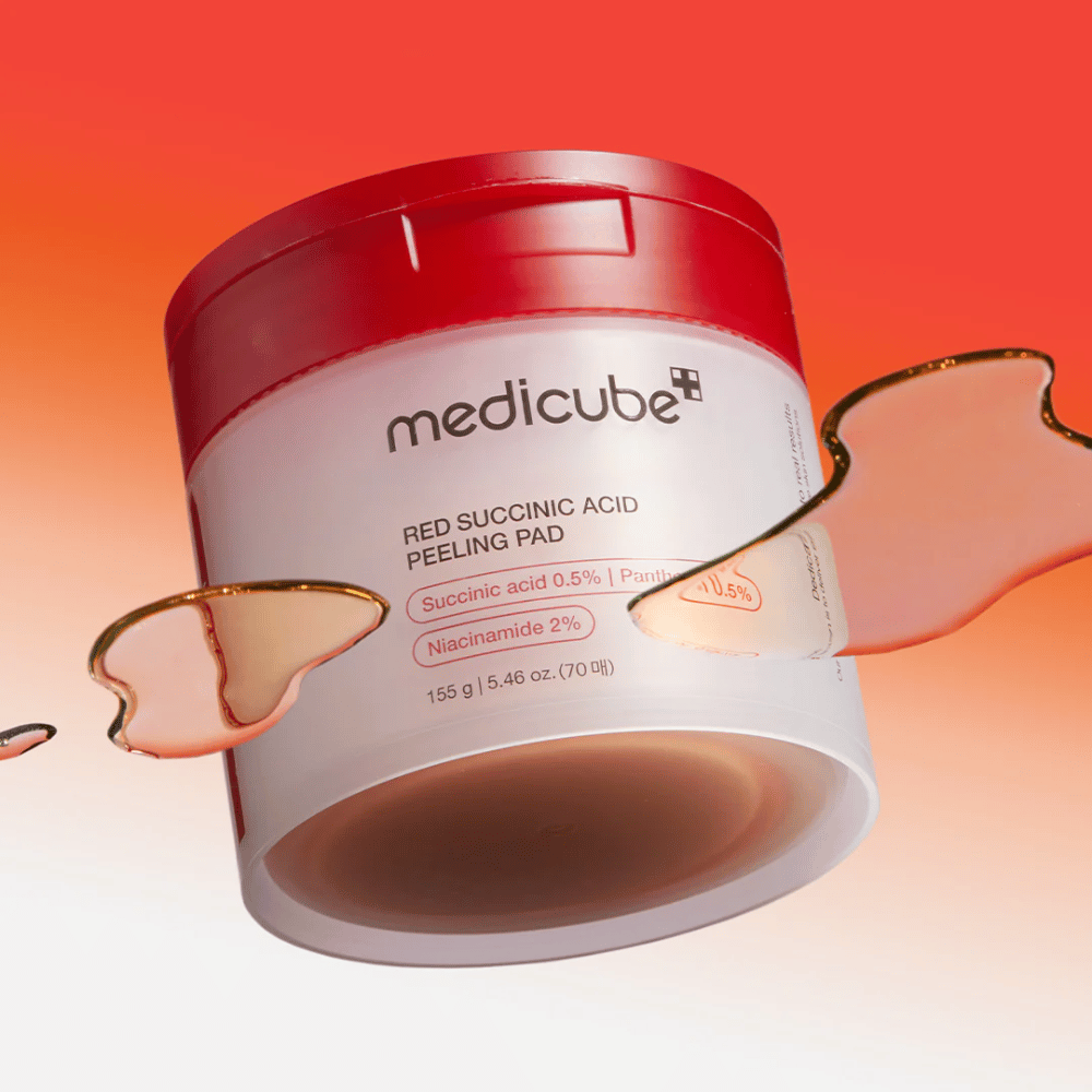 Medicube Red Succinic Acid Peeling Pad em um pote branco e vermelho, colocado contra um fundo degradê em vermelho e laranja. O produto contém ácido succínico e niacinamida para esfoliação e melhoria da pele. Textura líquida visível ao redor do pote.