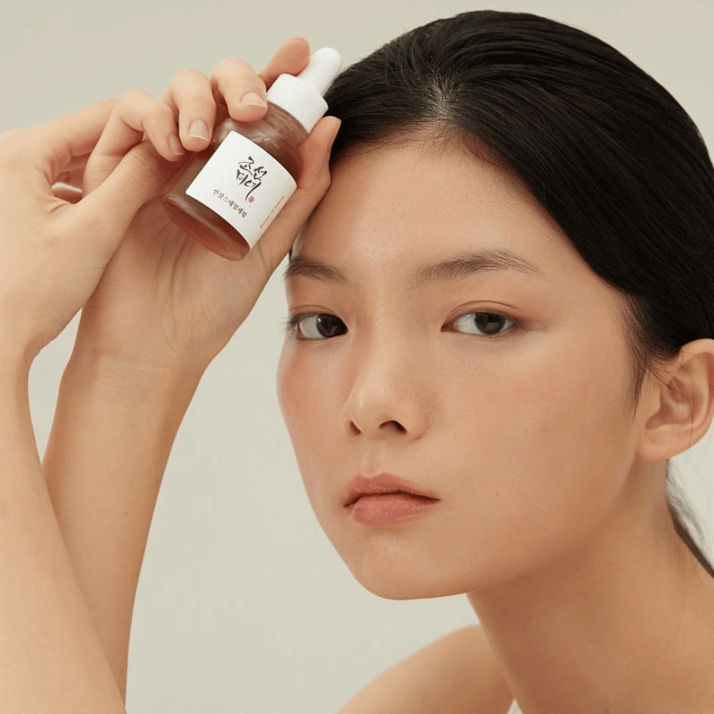 Modelo segurando Beauty of Joseon Revive Serum na bochecha – sérum nutritivo com ginseng e snail mucin.