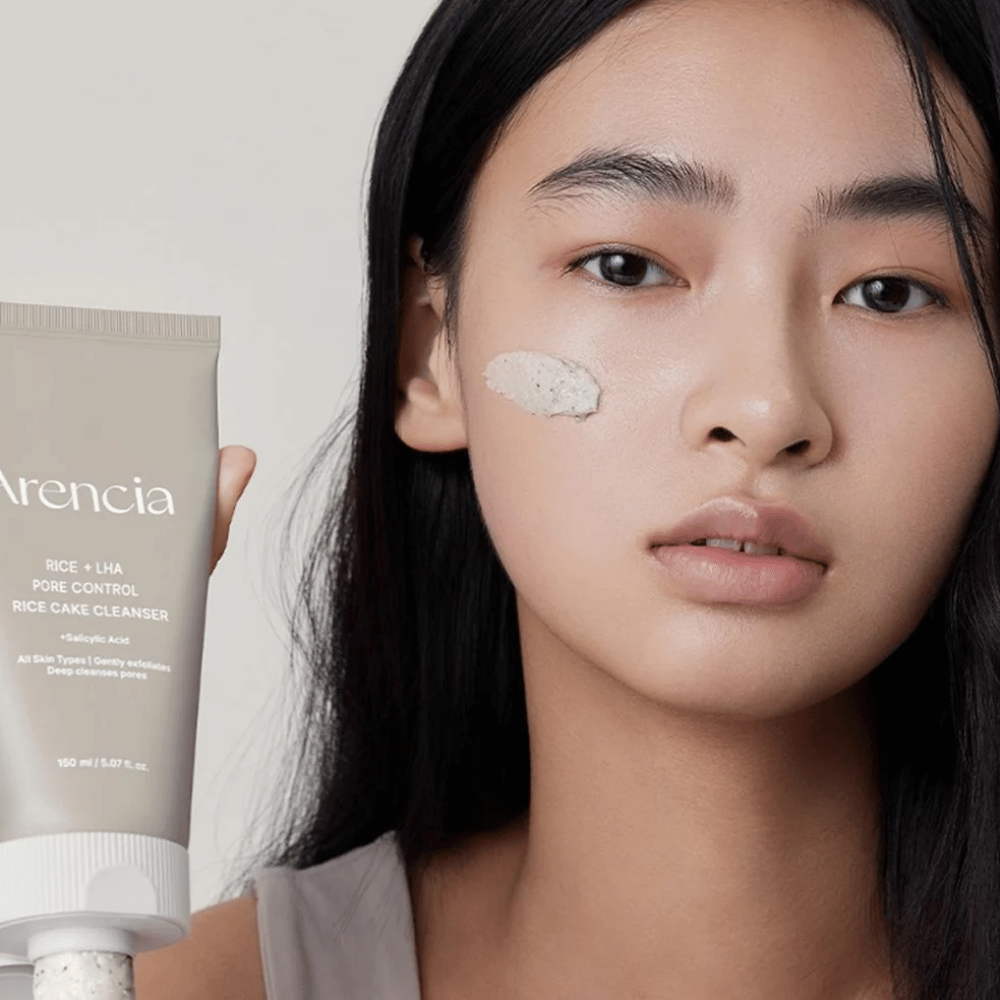Modelo segurando Arencia Rice + LHA Pore Control Rice Cake Cleanser com produto aplicado na bochecha, ilustra limpeza de poros suave mas eficaz para uso diário.