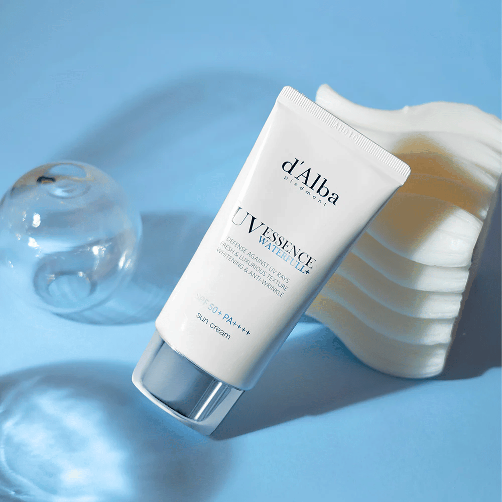 d'Alba UV Essence Waterfull+ Sun Cream com SPF 50+ PA++++ está sobre um fundo azul com reflexos de luz e elementos decorativos – destaca as propriedades frescas e hidratantes do protetor solar.
