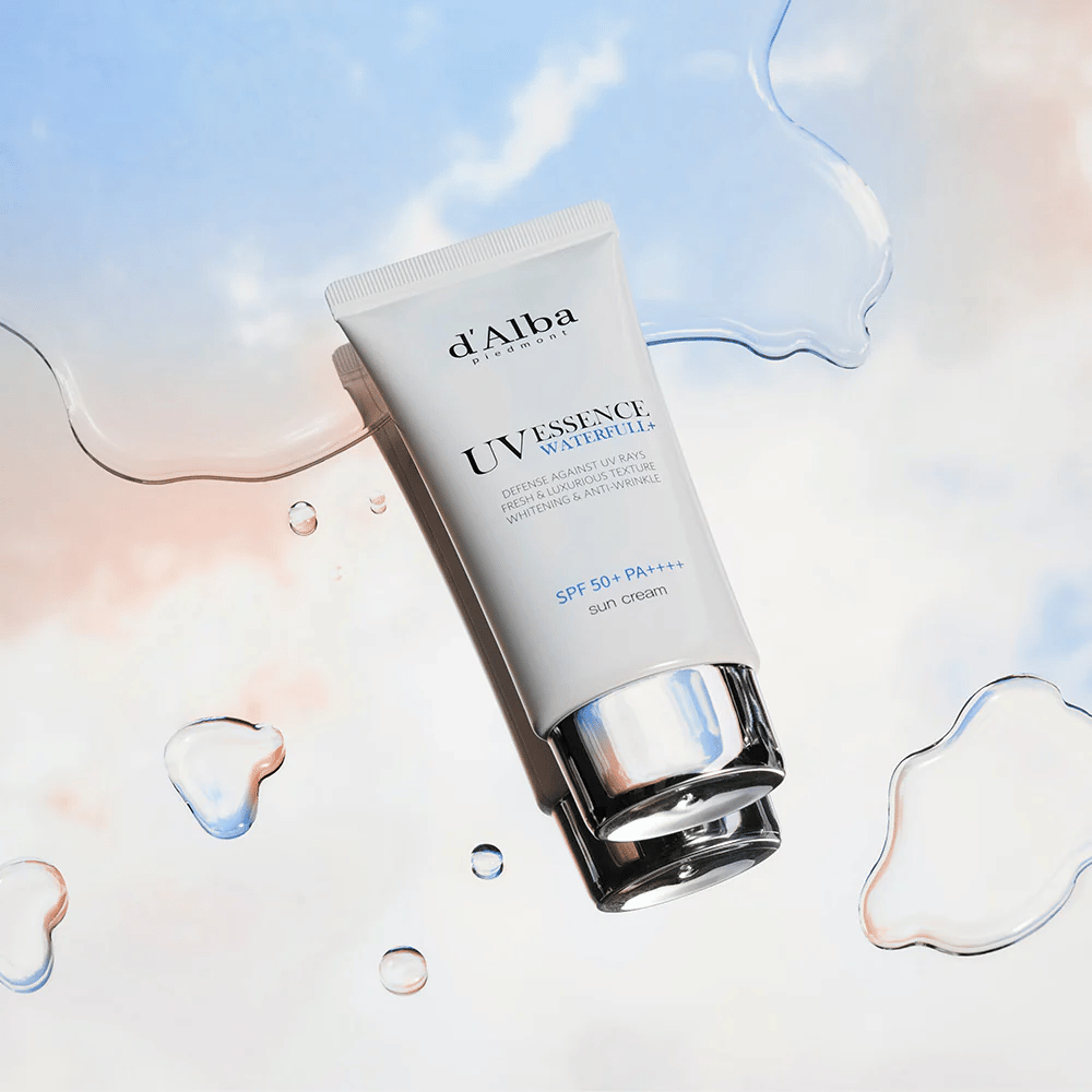 Imagem do produto d'Alba UV Essence Waterfull+ Sun Cream com SPF 50+ PA++++, colocada contra um fundo com respingos de água e céu azul-rosa – simboliza proteção solar leve e hidratante.