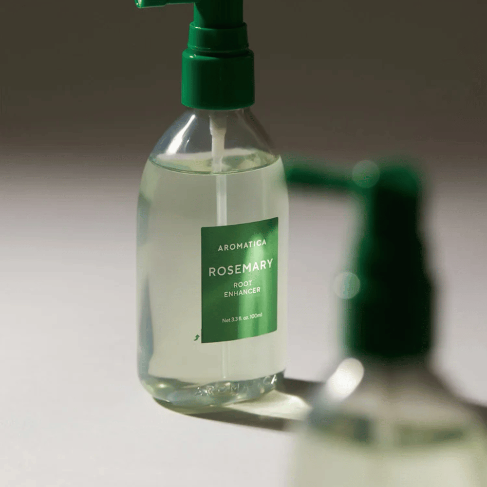 Grande plano de AROMATICA Rosemary Root Enhancer com aplicador de bico verde. A imagem foca-se no design do frasco e na aplicação precisa diretamente no couro cabeludo.