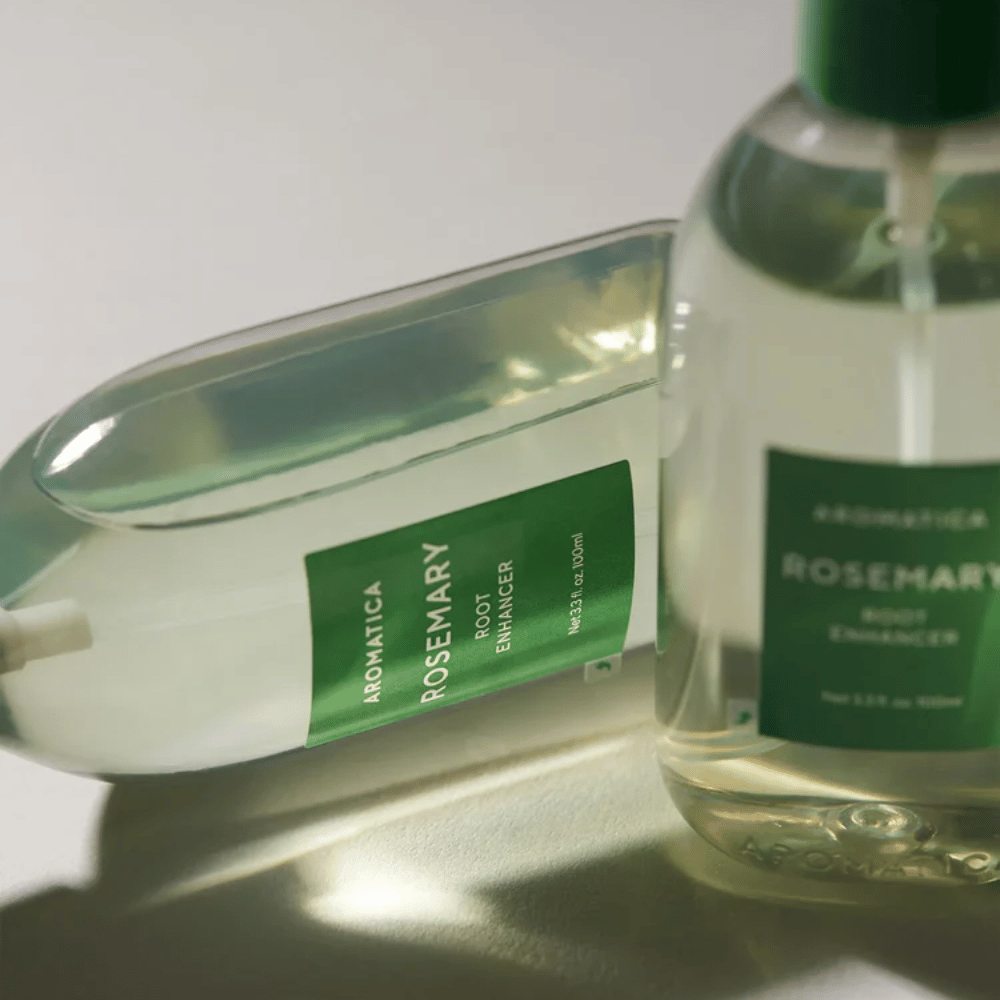 Dois frascos de AROMATICA Rosemary Root Enhancer com tampa protetora transparente e rótulo verde. Grande plano que destaca o design premium do produto e o conceito de cuidados capilares naturais.