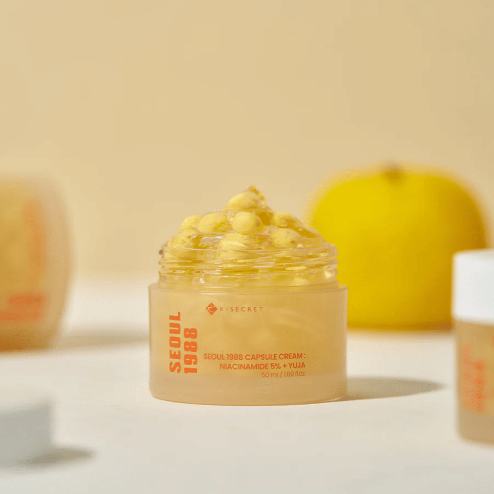 Frasco aberto com cápsulas amarelas ao lado de uma fruta yuja cortada ao meio que destaca a fórmula rica em vitamina C.