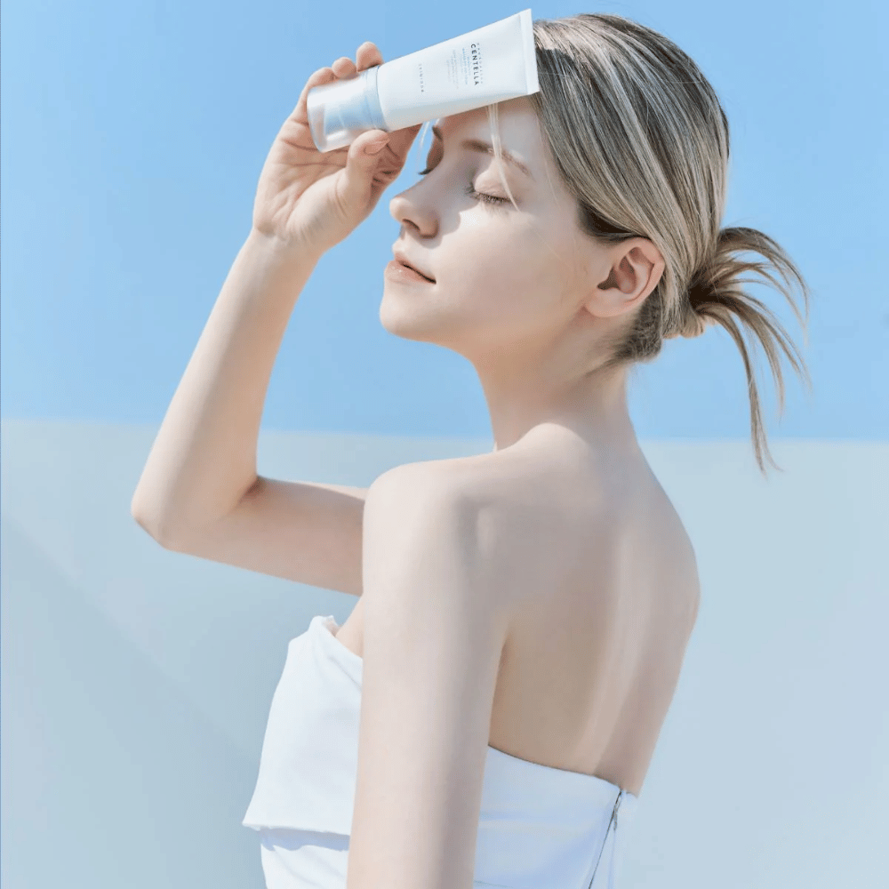 Uma mulher aplica SKIN1004 Madagascar Centella Hyalu-Cica Water-Fit Sun Serum 50ml para proteger o rosto dos raios UV.