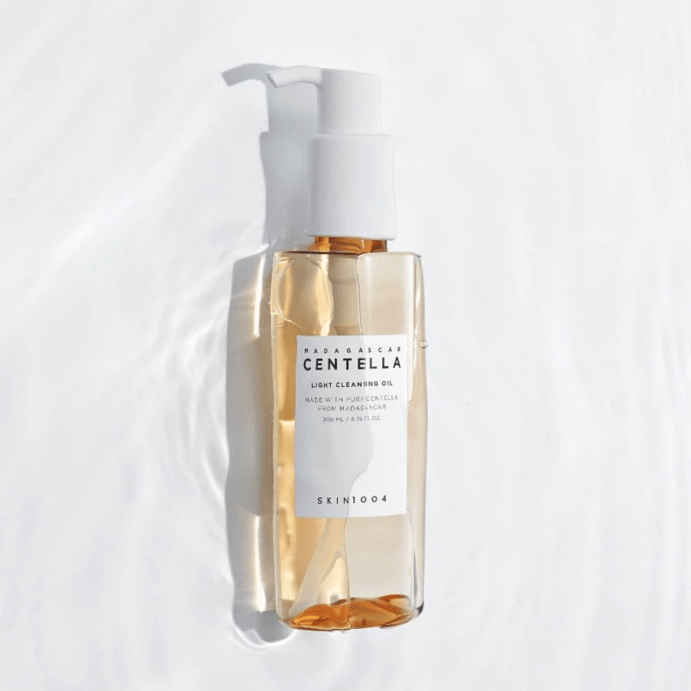 SKIN1004 Madagascar Centella Light Cleansing Oil em fundo branco com suaves reflexos de água que destacam o frasco transparente e o conteúdo dourado.