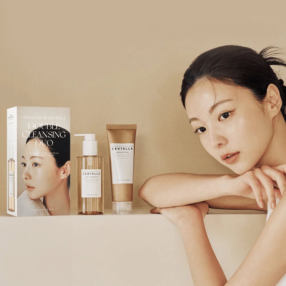 SKIN1004 Madagascar Centella Double Cleansing Duo Set com caixa, limpeza à base de óleo, espuma de limpeza e modelo com pele hidratada contra fundo bege.