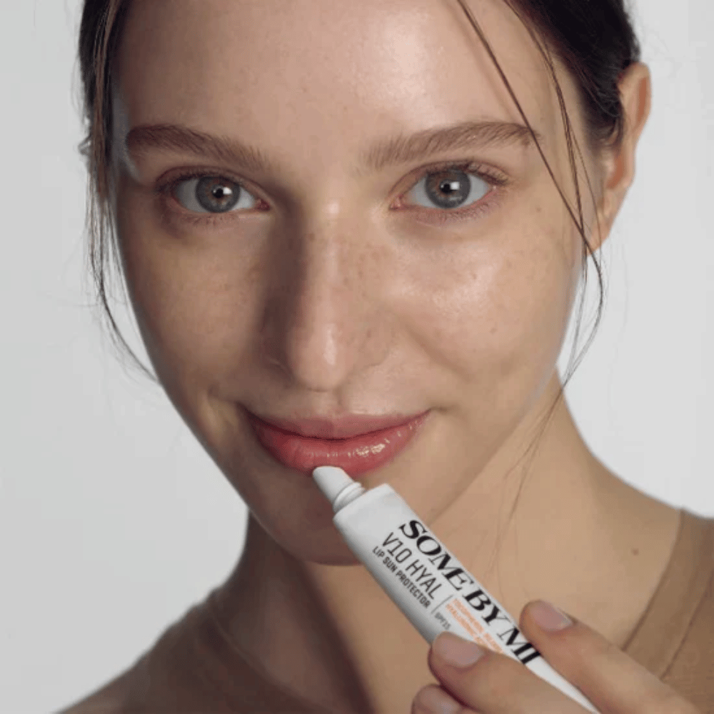 Uma mulher segura um tubo V10 Hyal Lip Sun Protector SPF15 de 7ml de bálsamo labial para proteção solar e hidratação, da SOME BY MI.