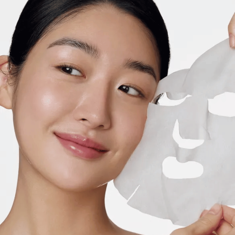 A imagem mostra uma pessoa a usar uma máscara facial, especificamente uma "Retinol Intense Daily Mask" da Some By Mi. A máscara é projetada para uso diário e contém retinol para melhorar a textura da pele, reduzir linhas finas e proporcionar um tom de pele mais uniforme.