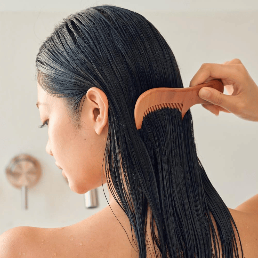 Pessoa penteia cabelo comprido e molhado com um pente de dentes largos após a aplicação de Heveblue Salmon Pullkeratin Centella Hair Treatment. Ilustra o efeito desembaraçante e suavizante para um resultado mais liso.