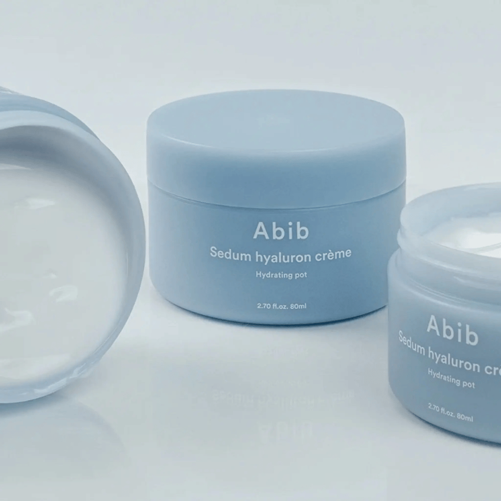 Três frascos de Abib Sedum Hyaluron Crème Hydrating Pot 80 ml em design minimalista azul claro, dos quais um frasco aberto mostra a consistência cremosa branca.