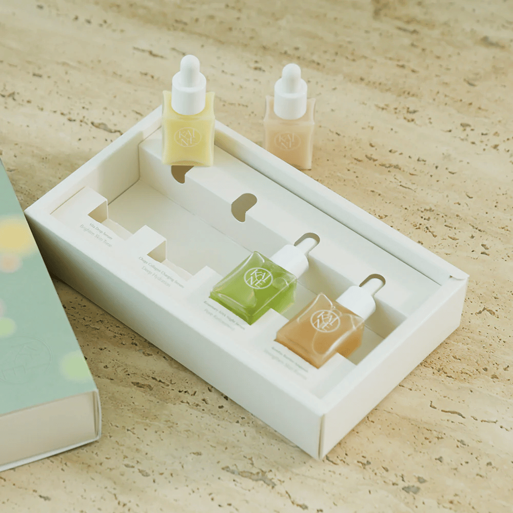 Quatro frascos de soro coloridos da KAINE Serum Discovery Kit com tampa de pipeta, projetados para atender diferentes necessidades da pele em uma embalagem minimalista e elegante.