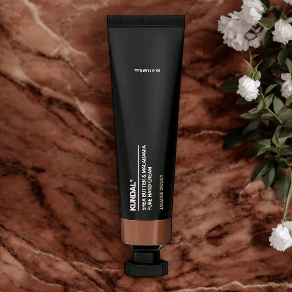 KUNDAL Shea Butter & Macadamia Pure Hand Cream Jasmine Woody colocado sobre mármore com flores – creme de mãos nutritivo que cuida das mãos secas e oferece uma elegante fragrância de jasmim amadeirado.