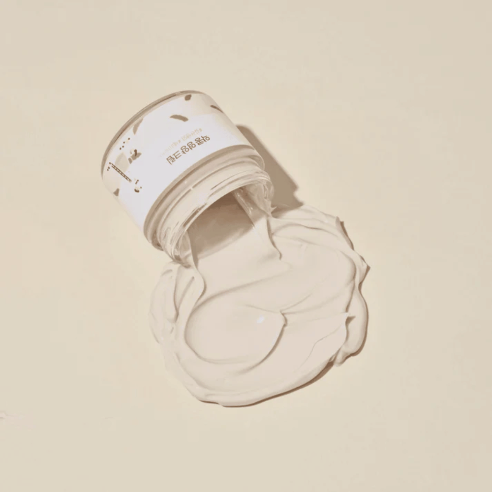 Mixsoon Soybean Nourishing Cream derramado do frasco sobre um fundo bege. A consistência rica do creme mostra suas propriedades hidratantes intensivas.