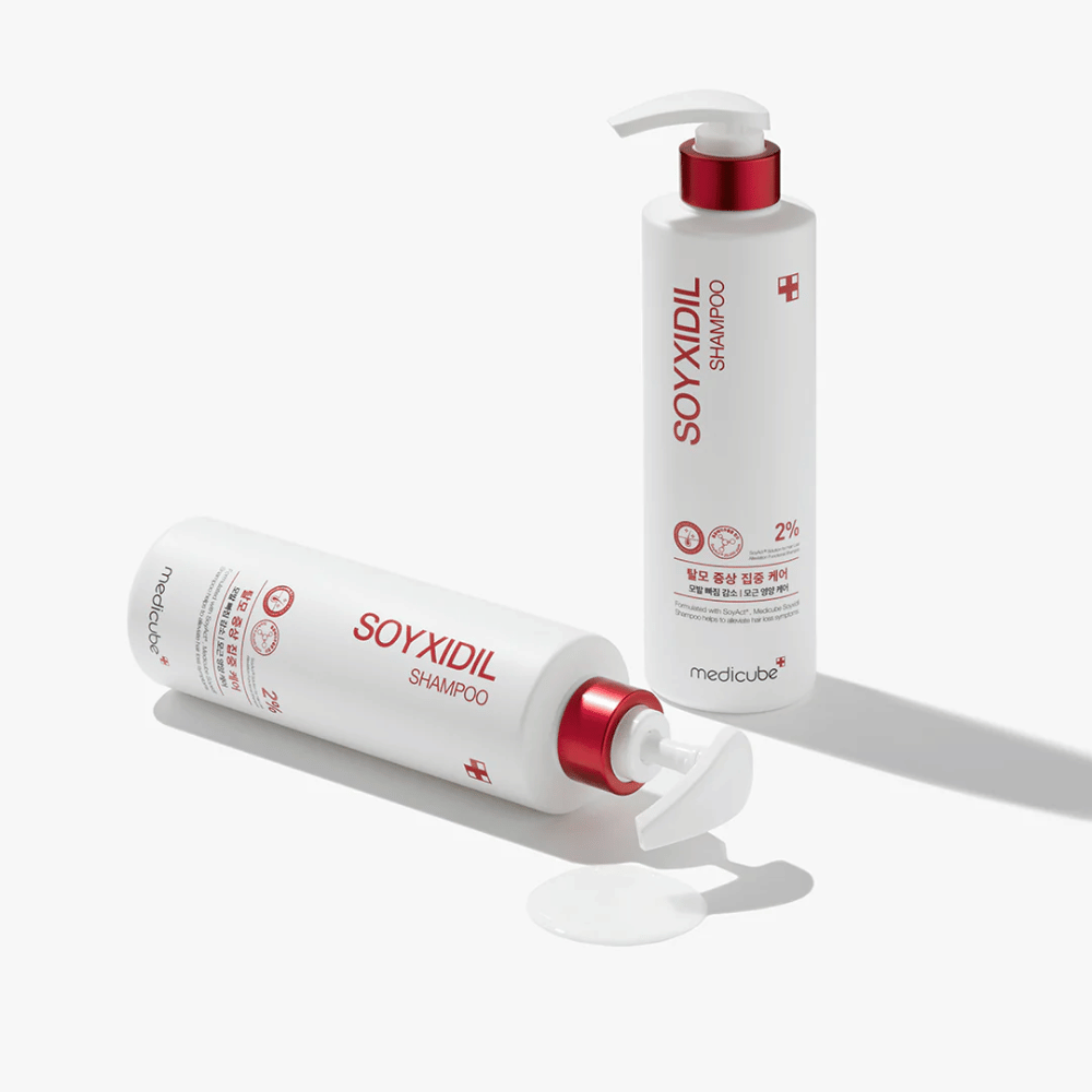 Duas garrafas de Medicube Soyxidil Shampoo em design branco e vermelho, uma em pé e outra deitada com champô derramado ao lado.