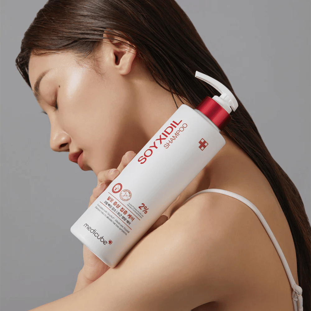 Mulher com cabelo comprido inclina a cabeça contra uma garrafa de Medicube Soyxidil Shampoo, que fortalece o couro cabeludo e combate a queda de cabelo.