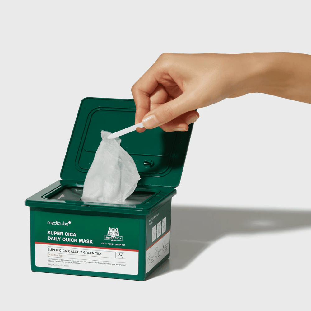 Recipiente verde com tampa aberta mostra medicube Super Cica Daily Quick Mask. Uma mão puxa uma máscara de folha com a pinça fornecida. O produto contém Cica, aloe e chá verde, ideal para hidratação rápida e efeito calmante.